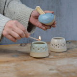 Bird match pot being held with match lighting tealight
