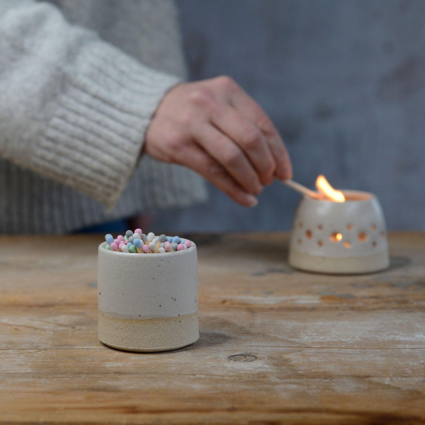 White match pot with pastel matches and tealight being lit in the background