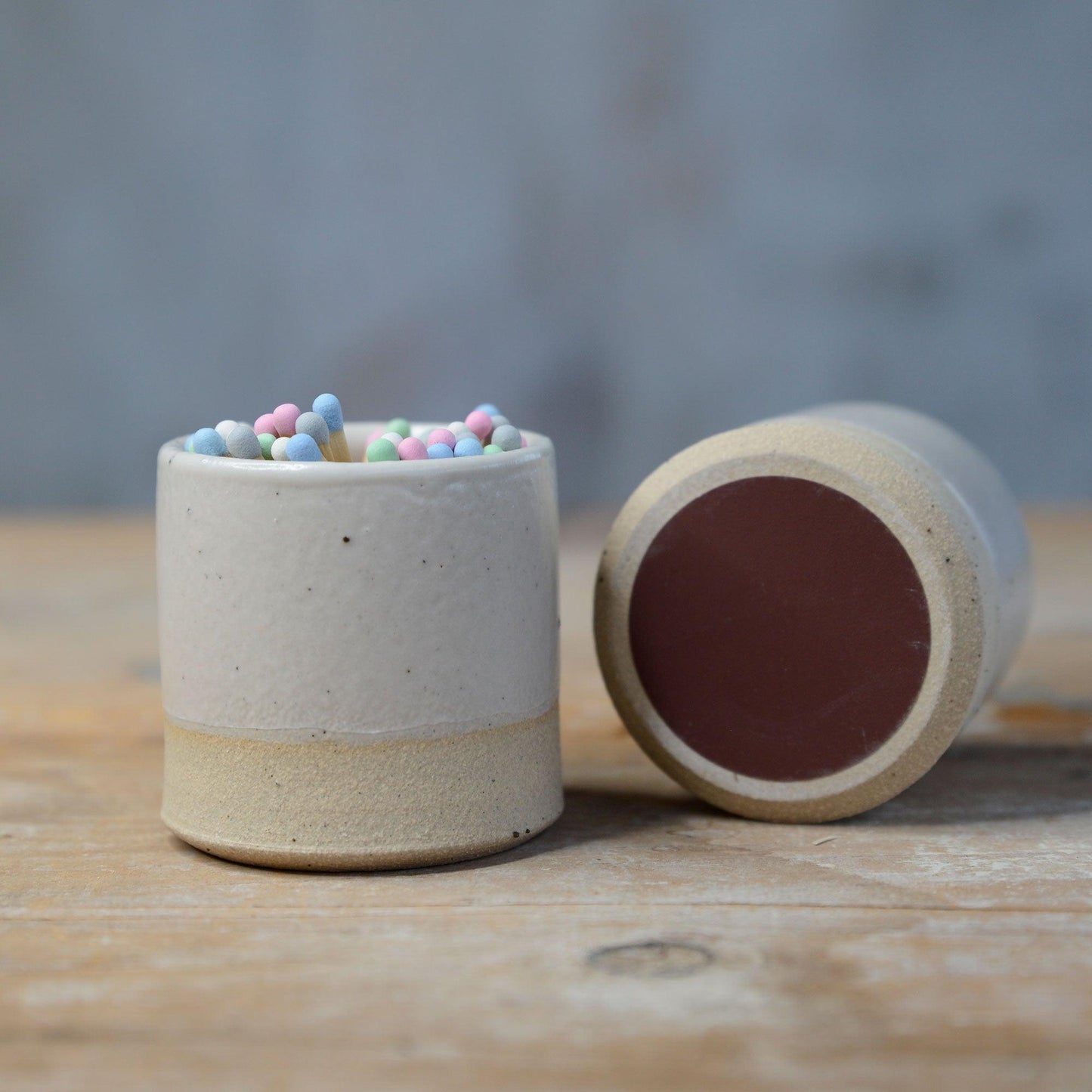 2 white match pots, one on its side showing the underside striker pad