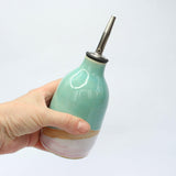 A hand holding the oil pourer for size reference