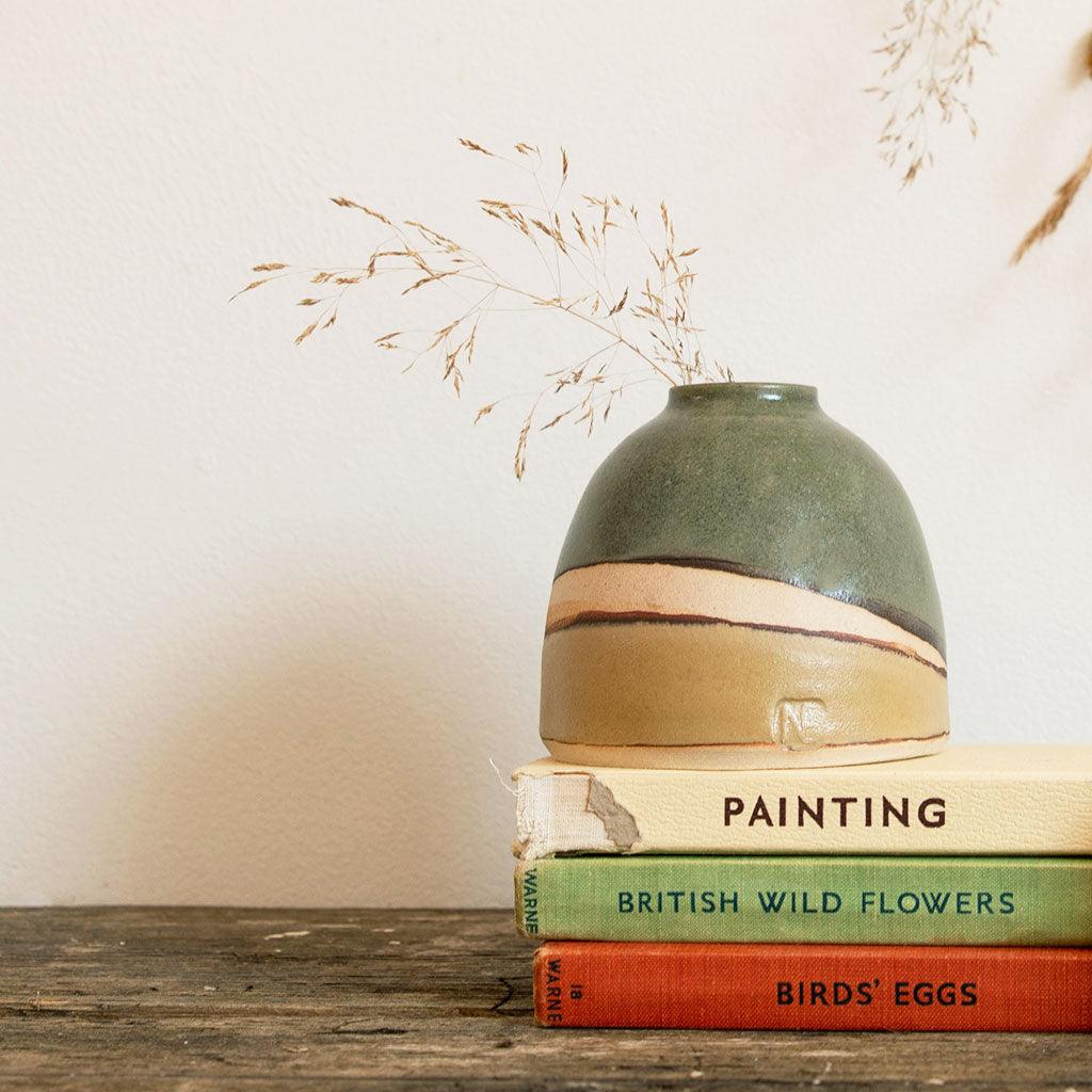 Dome Vase Moorland filled with dried seed stems on top of cream, green and red vintage books on a dark wooden surface