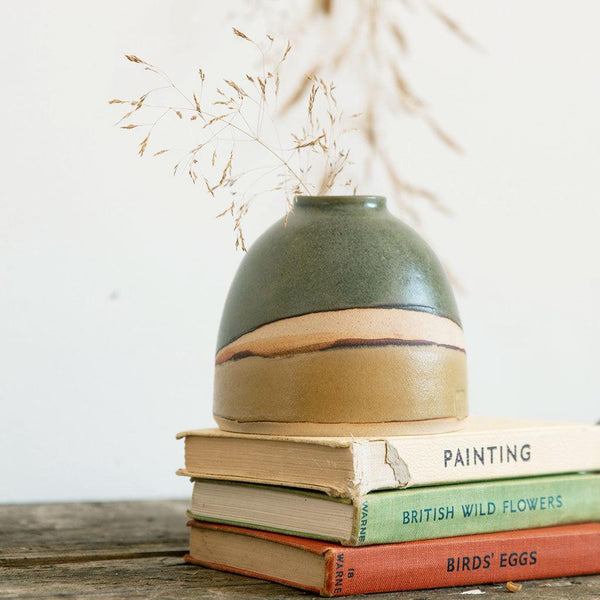 Close up side view of the Dome Vase Moorland on the stack of vintage books, showing the satin green and light brown-yellow glaze with exposed clay inbetween