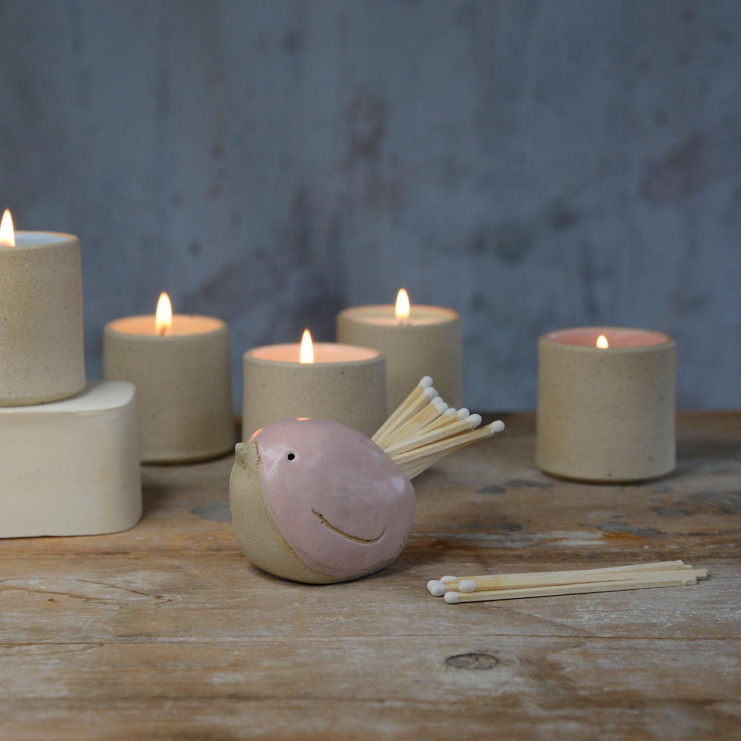 Pink bird pot filled with white matches in front of lit stoneware candles