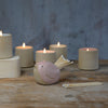 Pink bird pot filled with white matches in front of lit stoneware candles