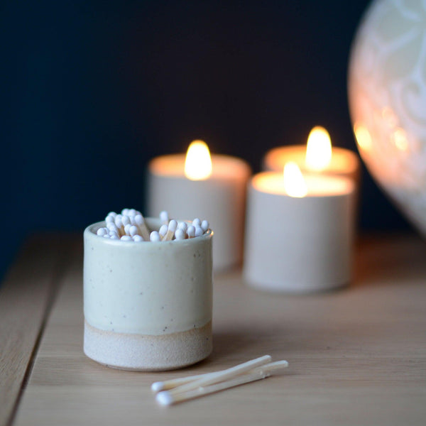 Yellow match pot with white matches on mantlepiece in front of lit candles