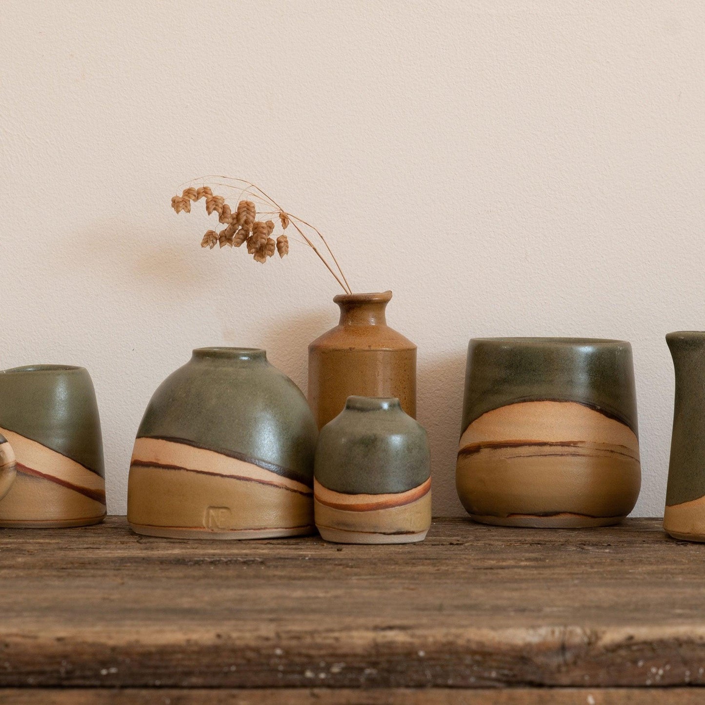 Moorland vases next to a Moorland tumbler and a pinch jug. A brown vase sits behind them with some dried seed stems in.