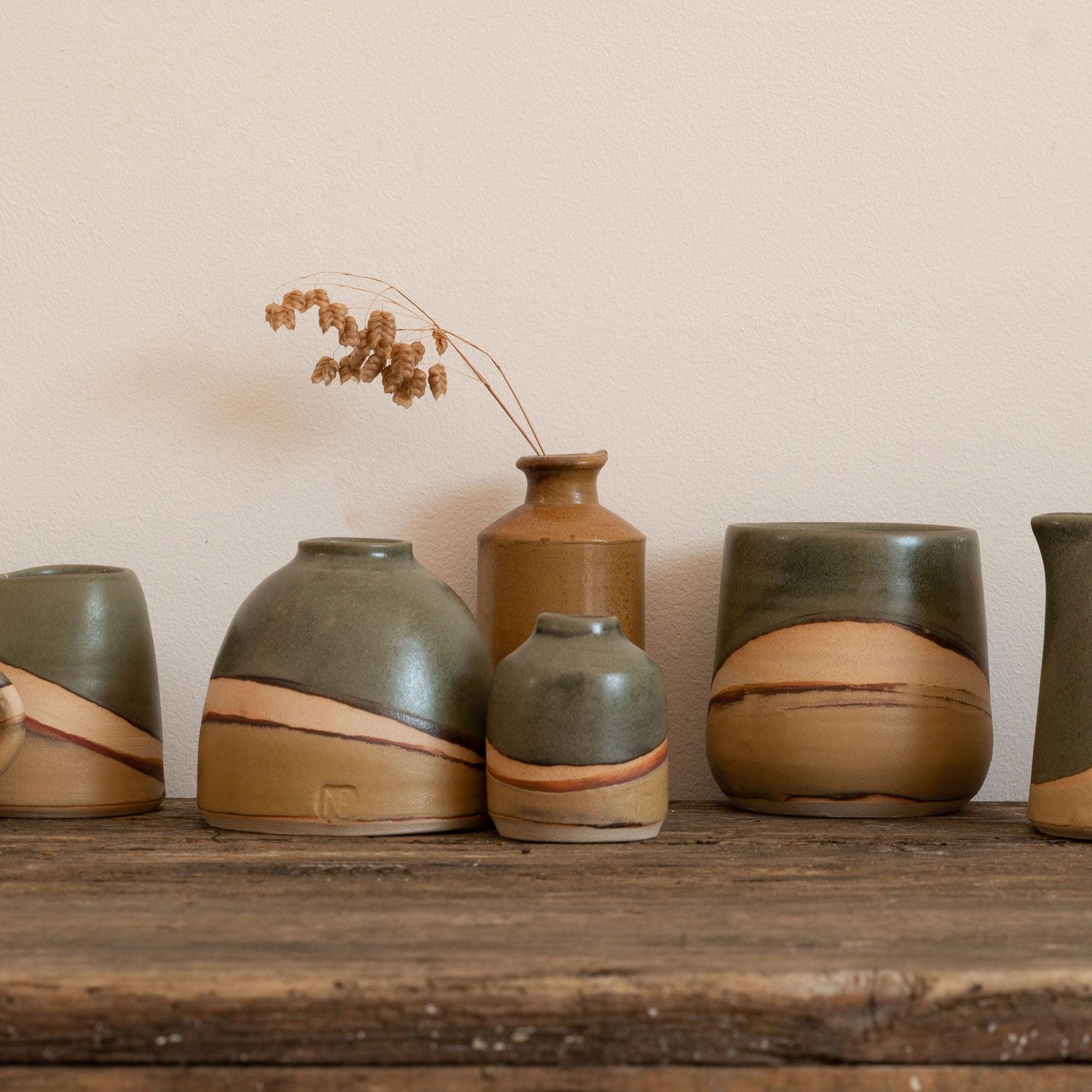 Moorland vases next to a Moorland tumbler and a pinch jug. A brown vase sits behind them with some dried seed stems in.