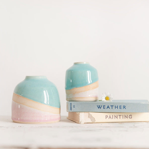 Shoreline dome vase next to a shoreline mini vase on a couple of pastel vintage books with a daisy flower on top