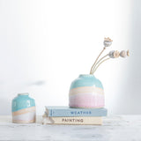 Shoreline dome vase filled with three dried poppy head stems on a couple of pastel vintage books, a mini shoreline vase sits to the left.