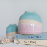 Close up of the pink glaze showin the pale to darker pink gradient against the exposed clay with a rim of orange burnoff. A mini Shoreline vase sits in the background