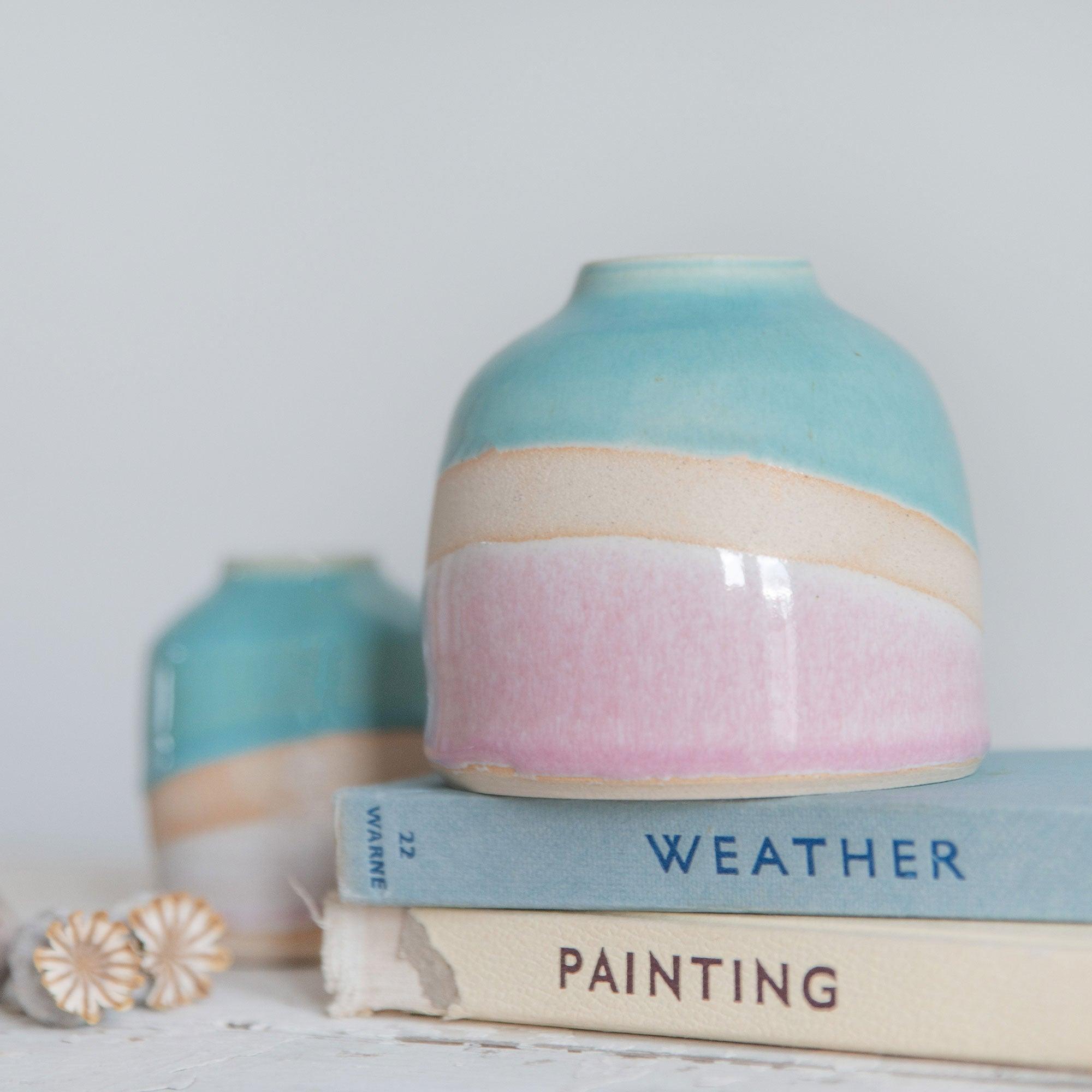 Close up of the pink glaze showin the pale to darker pink gradient against the exposed clay with a rim of orange burnoff. A mini Shoreline vase sits in the background