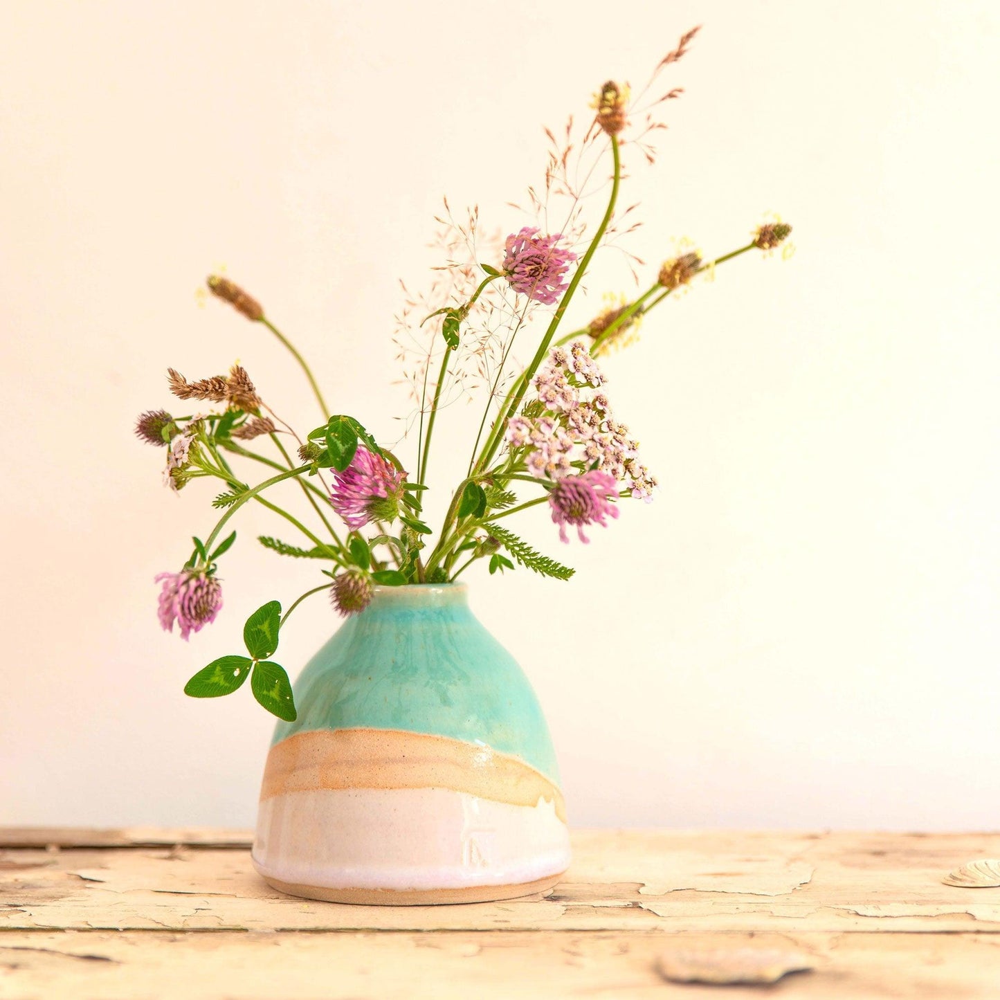 Shoreline dome vase with a glossy turquoise glaze and light gradient pink glaze with exposed clay. The vase is filled with a mixture of pink and green wildflowers.
