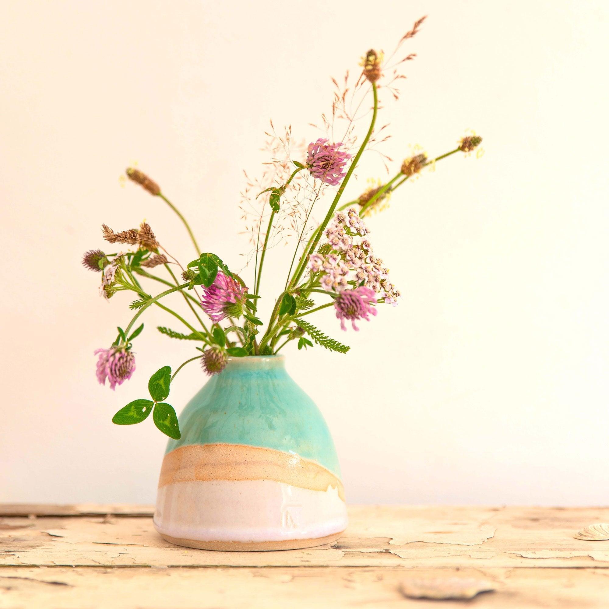 Shoreline dome vase with a glossy turquoise glaze and light gradient pink glaze with exposed clay. The vase is filled with a mixture of pink and green wildflowers.