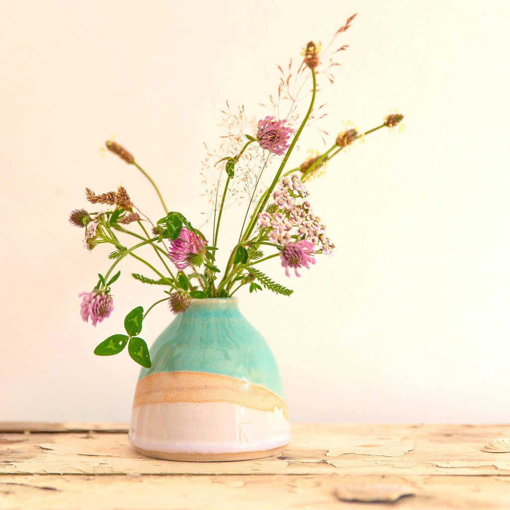 Shoreline dome vase with a glossy turquoise glaze and light gradient pink glaze with exposed clay. The vase is filled with a mixture of pink and green wildflowers.