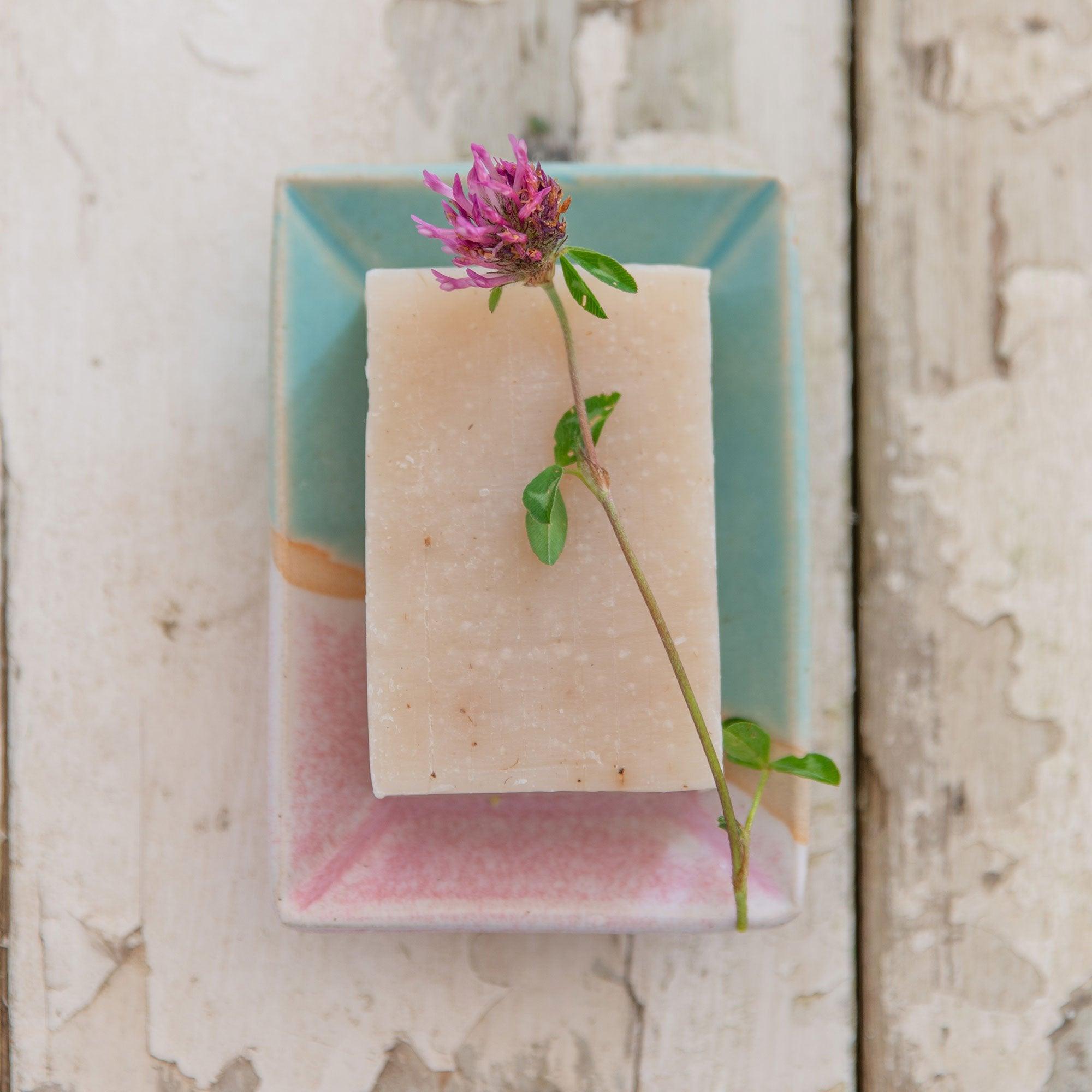 A pink wildflower sits on top of a bar of soap in the Shoreline soap dish