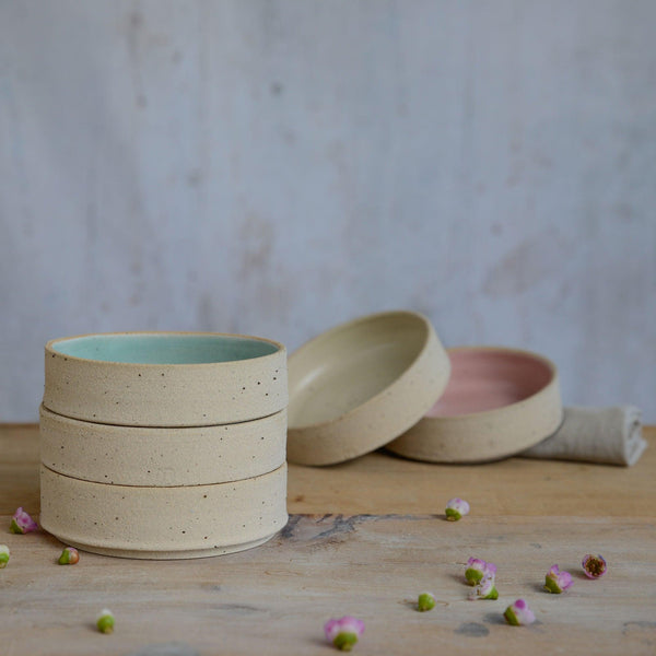 Stack of three bowls in foreground and pink and yellow bowls in background